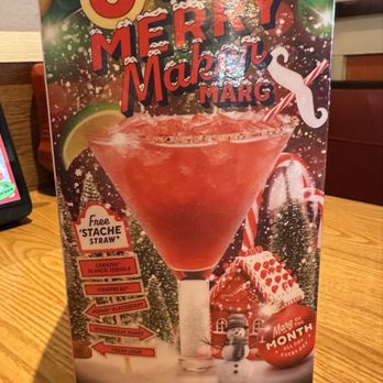 Chili's - Merry Maker Marg (seasonal) - A promotional menu displays a seasonal margarita called 'Merry Maker Marg' at Chili's, priced at $6. The menu features holiday-themed decorations including Christmas ornaments, snowflakes, and a gingerbread house. The drink is garnished with lime and served in a large glass with a free 'stache straw' offer. Additional ingredients listed include Blanco tequila, Cointreau, and strawberry puree. The background includes festive elements like a snowman and Christmas trees, emphasizing the holiday promotion. - Bars Near Me - Lone Tree, Colorado