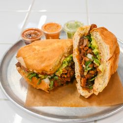 Gus Tacos - Torta: Served in a bun with beans, cheese, guacamole, chipotle mayo, onions, cilantro and your choice of protein.