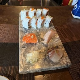 Salmon Roll - A marble serving board holds assorted sushi, including rolls topped with fish roe, sashimi slices, and pickled ginger, at a restaurant.