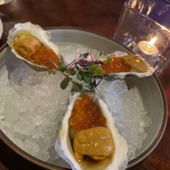 Tavern 157 - Oysters with uni - Three oysters with uni and salmon roe are presented on a bed of ice, garnished with microgreens, in a restaurant setting with a candle nearby. - Lounges Near Me - Flushing, New York