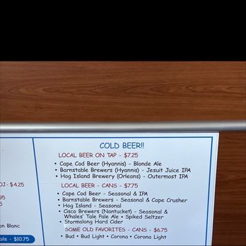 Hy-Line Cruises - Beer options - The image shows a menu board with a list of beer options, including local beers on tap, canned beers, and some old favorites, along with their prices. The menu is organized into sections with headings such as 'Cold Beer!!', 'Local Beer - Cans', and 'Some Old Favorites - Cans'. The background includes a wooden surface at the top, and the menu is framed with a metallic border. The focus is on the text and beer options available for purchase. - Transportation Near Me - Hyannis, Massachusetts