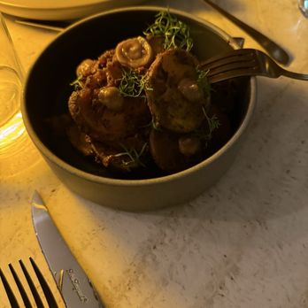 Taline - Potato - A bowl of roasted potatoes topped with herbs and a creamy sauce, placed on a marble table with cutlery nearby. - Mediterranean Near Me - Toronto, Ontario