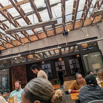 Pilsen Yards - Another area next to the covered patio with more art. - Diners are seated at tables inside a restaurant with a high, open ceiling featuring exposed wooden beams and string lights. - Tacos Near Me - Chicago, Illinois