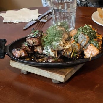 Lola - Duroc Pork, Washington Chicken, and Bristol Bay Sockeye Salmon Kebabs on a sizzling skillet at Lola in Seattle. - Greek Near Me - Seattle, Washington Lola - Duroc Pork, Washington Chicken, and Bristol Bay Sockeye Salmon Kebabs on a sizzling skillet at Lola in Seattle. - Greek Near Me - Seattle, Washington