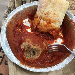 Meatballs - A foil container holds a meatball covered in marinara sauce, with a piece of bread on top, on a paper-lined surface.