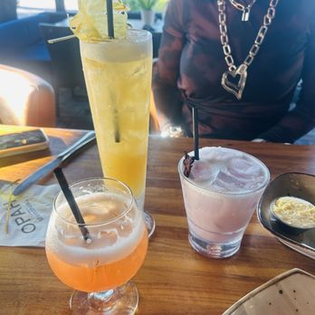OPAH Seafood Grill - Koloa pineapple cooler in the tall glass, the purple one is the Iris margarita and the orange drink is the coco jungle. All - New American Near Me - Aliso Viejo, California OPAH Seafood Grill - Koloa pineapple cooler in the tall glass, the purple one is the Iris margarita and the orange drink is the coco jungle. All - New American Near Me - Aliso Viejo, California