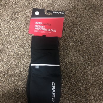 Fleet Feet - A black CRAFT hybrid weather glove with a white zipper and label is placed on a brown carpet. The glove is designed for cold weather activities. - Sports Wear Near Me - Buffalo, New York