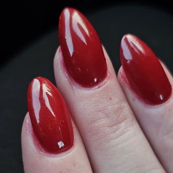 Ivy Nails & Spa - A close-up image features three fingers with well-manicured nails painted in glossy red polish. The nails are shaped with a pointed oval tip and reflect light, indicating a smooth, shiny finish. The skin around the nails appears natural, and the background is dark, emphasizing the vibrant color of the nails. - Nail Salons Near Me - Middleton, Massachusetts