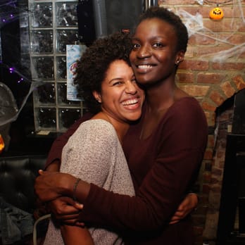 Metropolitan - a woman hugging another woman in a living room - Gay Bars Near Me - Brooklyn, New York Metropolitan - a woman hugging another woman in a living room - Gay Bars Near Me - Brooklyn, New York
