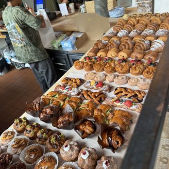 Le Petit Monstre - Pastries - A bakery counter showcases a variety of pastries such as croissants, danishes, and cream-filled pastries, with a staff member and customer in the background. - Patisserie/Cake Shop Near Me - Brooklyn, New York