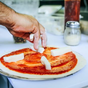 Sfila Pizza - a person putting cheese on a pizza - Pizza Near Me - New York, New York Sfila Pizza - a person putting cheese on a pizza - Pizza Near Me - New York, New York