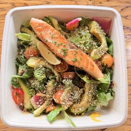 Voyage salad with salmon and sesame soy sauce - A salmon fillet is placed on a mixed salad with vegetables, cherry tomatoes, avocado, radish, and lemon wedge, topped with sesame seeds and chopped chives.