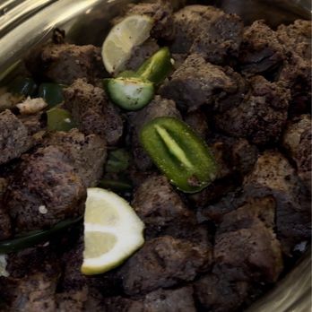 De Afghanan - Cooked meat chunks with lemon wedges and sliced green chili peppers in a stainless steel serving dish. - Afghan Near Me - Tracy, California