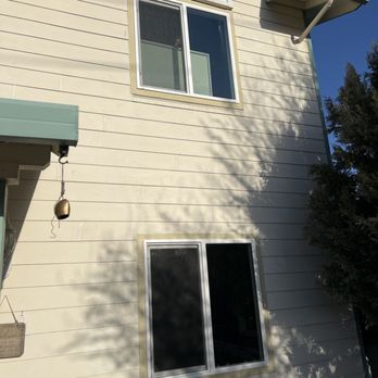 High Performance Roofing - Both new windows - The image shows two newly installed windows on a beige house exterior, with the upper window featuring decorative arch trim. - Roofing Near Me