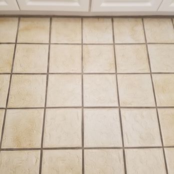 The Groutsmith - This image shows a close-up of light-colored floor tiles with dark, possibly discolored grout lines underneath white kitchen ... - Grout Services Near Me - Sarasota, Florida