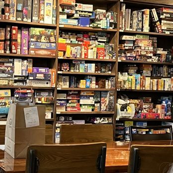 House Rules - a woman sitting at a table in front of a bookshelf - Tabletop Games Near Me - Grand Rapids, Michigan