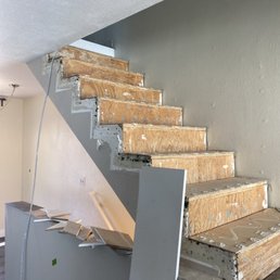 The stairs before any work had been done - The image shows a staircase with wooden steps in the process of renovation, with drywall partially removed and construction debris present.