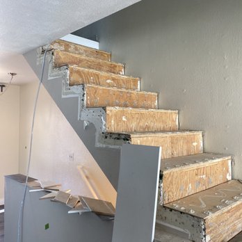 Fix It Nick - The stairs before any work had been done - The image shows a staircase with wooden steps in the process of renovation, with drywall partially removed and construction debris present. - Handyman Near Me
