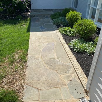 CM Hardscapes - Front walkway - A stone pathway runs alongside a garden bed with shrubs and plants, leading to a house entrance in Arlington, VA. - Masonry/Concrete Near Me
