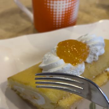 Ganache Bakery - Delicious mango delight! - A dessert plate features a lemon cake topped with whipped cream and jam, with a cup of black coffee in the background on a wooden table. - Bakeries Near Me - Morton Grove, Illinois
