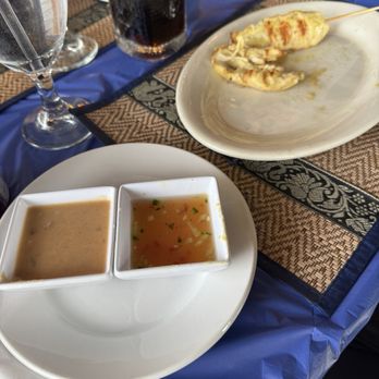 Pha Khao - Chicken satay - A plate with a chicken satay skewer, two dipping sauces, and drinks including a glass of water, a glass of soda, and a glass of champagne on a table. - Thai Near Me - Kenosha, Wisconsin