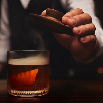 The Garrison - The Garrison signature cocktail combines The Manhattan and the Old Fashioned. It's served on a whiskey rock with hickory smoke. - New American Near Me - Ozark, Missouri The Garrison - The Garrison signature cocktail combines The Manhattan and the Old Fashioned. It's served on a whiskey rock with hickory smoke. - New American Near Me - Ozark, Missouri