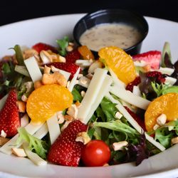 Uccello's - Downtown - Uccello's Riviera Salad with garden greens, strawberries, mandarin oranges, tomatoes, Swiss cheese, and cashews on a white pl...