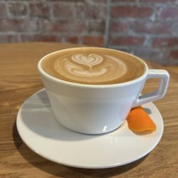 Commissary Barber & Barista - Latte on a wooden table with brick background in a white mug