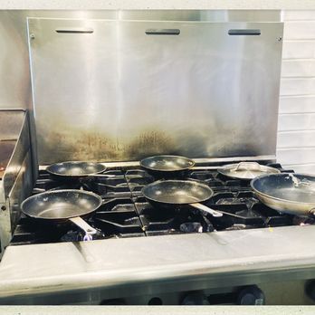 Toad in the Hole - Love a working kitchen- cooking with gas - A commercial kitchen stove features six small frying pans placed on the burners, with a deep fryer on the left side. The stove has a stainless steel surface and backsplash, with a white tiled wall behind it. A temperature control knob is visible on the deep fryer, and a gas line is connected to the stove. The setup indicates a professional cooking environment. - Breakfast & Brunch Near Me - Eagle River, Wisconsin