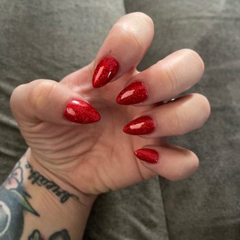 Oh La La Nail Spa - Acrylic Fill with No chip polish! - A hand with red glittery, almond-shaped nails is shown, with a tattooed wrist and a gray background. - Nail Salons Near Me - Elgin, Illinois
