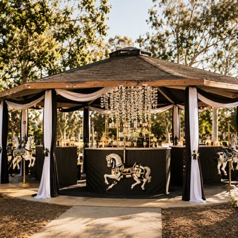 The Gathering Co - A fully activated carousel bar -- black & gold, draped in fabric, flanked by hand-painted carousel horses -- sitting inside a park gazebo. - Party & Event Planning Near Me The Gathering Co - A fully activated carousel bar -- black & gold, draped in fabric, flanked by hand-painted carousel horses -- sitting inside a park gazebo. - Party & Event Planning Near Me