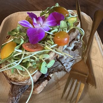 The Coffee Builders - Prime, pimento, and bleu Panini - A plated dish with a whole cooked fish topped with microgreens, edible purple flowers, cherry tomatoes, and bread slices, served on a wooden tray. - Coffee & Tea Near Me - Phoenix, Arizona