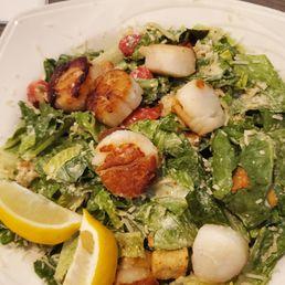 Scallop Caesar Salad - A Caesar salad featuring grilled scallops, chopped romaine lettuce, cherry tomatoes, croutons, and grated cheese, garnished with lemon wedges.