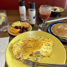 Cheese Omelette - A breakfast meal includes an omelette on a yellow plate, a side of fruit, and drinks such as juice and water, with condiments and additional food items in the background.