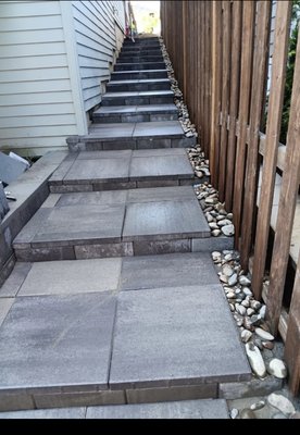 Custom Stepped Walkway & Side Yard Drainage - Transformed a steep, narrow side yard into a highly functional, safe walkway using large-format concrete pavers and durable concrete risers. Built-in river rock borders provide clean drainage to prevent hillside erosion and water pooling. Custom Stepped Walkway & Side Yard Drainage - Transformed a steep, narrow side yard into a highly functional, safe walkway using large-format concrete pavers and durable concrete risers. Built-in river rock borders provide clean drainage to prevent hillside erosion and water pooling.