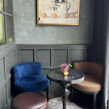 Truth Be Told - While you wait for a table. - A corner of a room features two upholstered chairs, one in blue and the other in brown, with a small round table between them, decorated with a flower arrangement. - Pubs Near Me - Chicago, Illinois