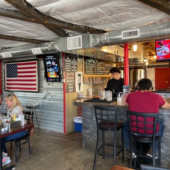 The 377 Brewery - people sitting at the bar - A casual brewery interior featuring a bar area with patrons seated, a chalkboard menu, and a large American flag on the wall. - Brewpubs Near Me - Albuquerque, New Mexico