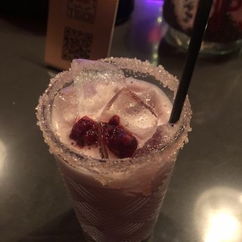 Common Tiger - Pink Pony Club (raspberry simple syrup, white chocolate, oat milk and egg white) - A pink-colored cocktail with ice cubes and red berries on top, served in a tall glass with a sugared rim and a black straw. - Speakeasies Near Me - Mission, Kansas
