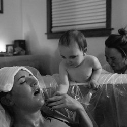 Beautiful Beginnings Homebirth - Mother in the birth tub with toddler holding her hand during labor
