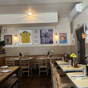 Beco - Inside Beco - A dining area with wooden tables and chairs, decorated with flowers, and framed pictures on the walls, in a restaurant setting. - Brazilian Near Me - Brooklyn, New York