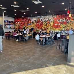Dining - A fast-food restaurant interior featuring a graffiti mural with cartoon characters and words, with customers seated at tables and some standing.