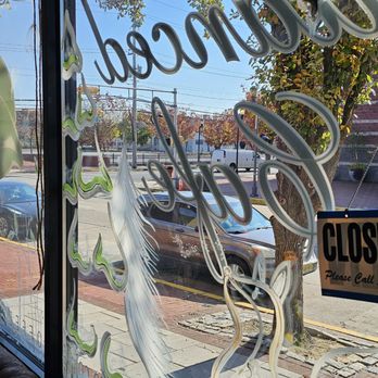 Nuanced Cafe - a view of the outside of the restaurant - A window with painted decorative designs, including a feather and tree, overlooks a street scene with trees, cars, and power lines. - Coffee & Tea Near Me - Camden, New Jersey