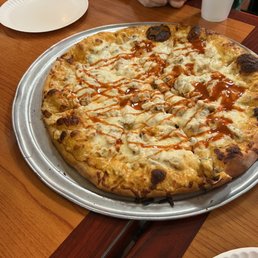 Yum - A large pizza topped with cheese, chicken pieces, and drizzled with sauce, served on a metal tray at a restaurant table.