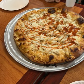 One Guy from Italy University - Yum - A large pizza topped with cheese, chicken pieces, and drizzled with sauce, served on a metal tray at a restaurant table. - Pizza Near Me - Lubbock, Texas