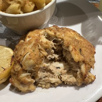 Mama's on the Half Shell - A plate features a partially cut fried chicken with visible stuffing, accompanied by a lemon wedge and a bowl of macaroni and cheese with breadcrumbs. - Bars Near Me - Baltimore, Maryland