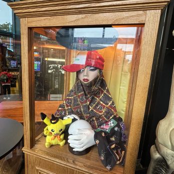 Bit Bar Salem - A mannequin wearing a kimono and a red cap is displayed inside a wooden case, holding a Pikachu plush toy. The setting appears to be inside a gaming or entertainment venue. - Bars Near Me - Salem, Massachusetts