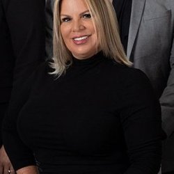 Tailored Realty - A woman with blonde hair and a black turtleneck smiles in a professional portrait. She is seated and appears to be part of a ...