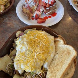 French Toast - A breakfast plate features scrambled eggs topped with shredded cheese, alongside toasted bread slices. A dessert with strawberries, whipped cream, and powdered sugar is also visible.