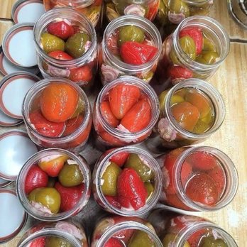 Carmella's Market - The perfect gift for the holidays - Multiple glass jars containing pickled red and green peppers are arranged on a wooden surface, with some open lids visible. - Cheese Shops Near Me - Boston, Massachusetts