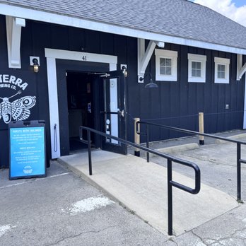 Nocterra Brewing - The image shows the front of Nocterra Brewing Co., a black building with a white logo of a moth, a ramp for accessibility, and a sign for guests with children. - Breweries Near Me - Powell, Ohio